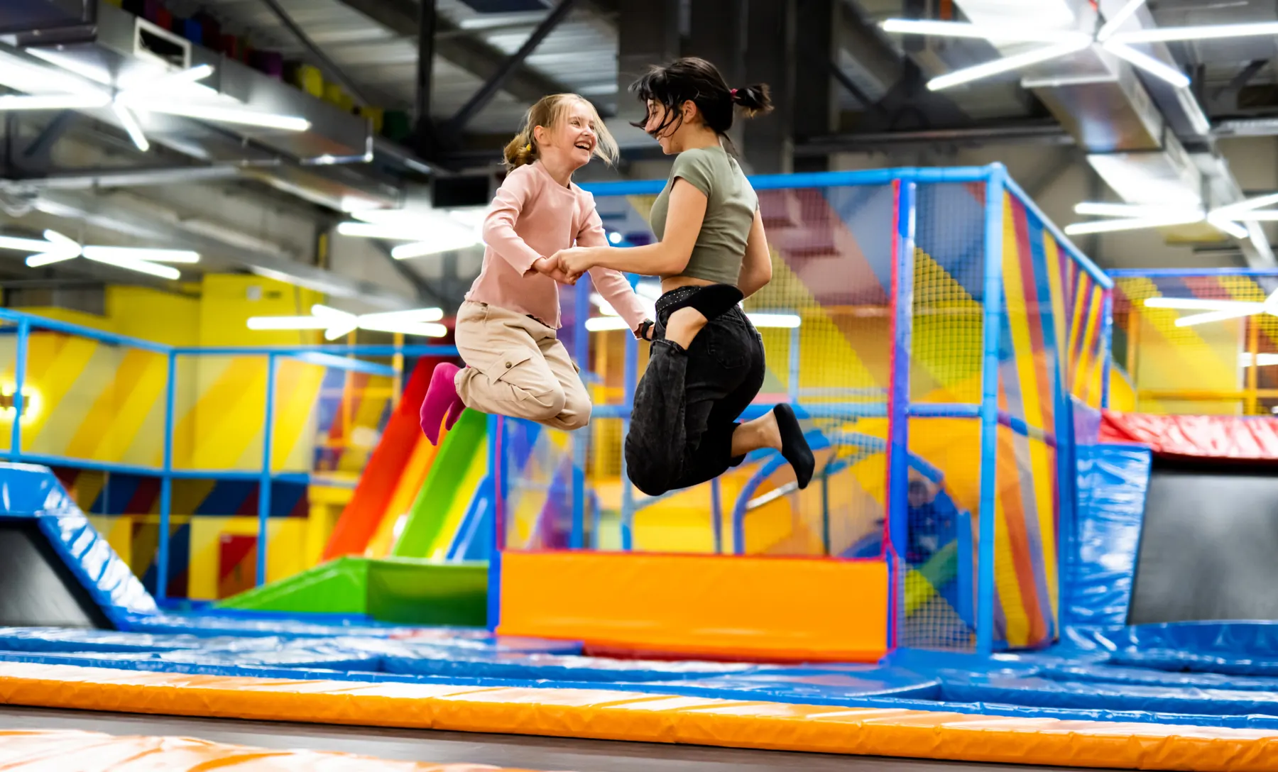 Una niña y una joven saltan tomadas de la mano en un parque de trampolines
